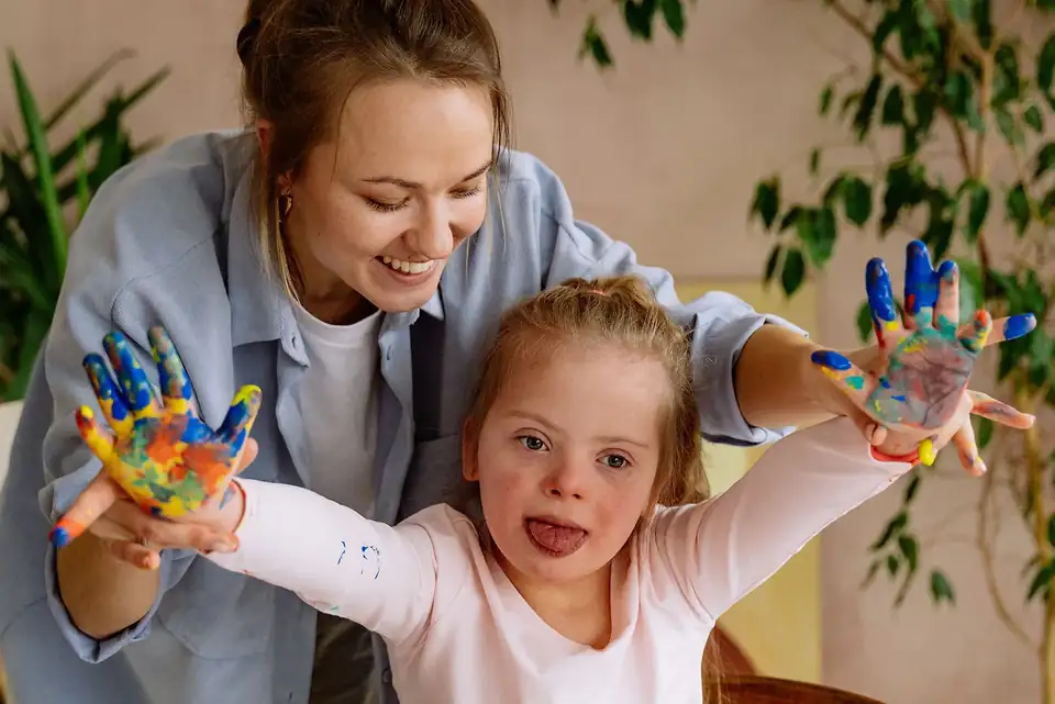 A support worker and a child with painted hands, both smiling